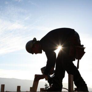 roofer wearing hard hat nails down shingles 